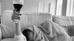 Ressaca de você: foto de uma mulher deitada, com o rosto coberto e segurando uma taça de vinho tinto